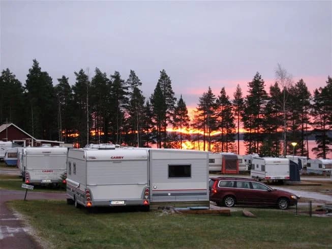 En bild som visar en campingplats på Sollerön, med husvagnar och husbilar parkerade i ett uppdelat område. Bakgrunden består av träd och ett öppet himmel.