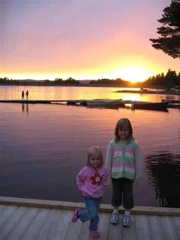 En lugn sjö med spegling av solnedgången på himlen, omgiven av silhuetter av träd i skymningen vid Sollerö camping.
