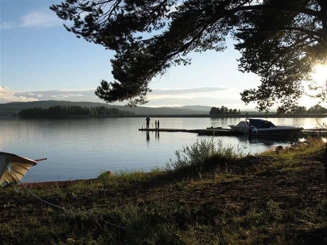 En solig dag vid Sollerö Camping med en vy över en glittrande sjö omgiven av frodig natur och ett par lätta moln på himlen.