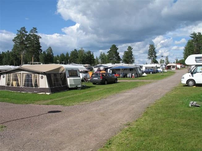 En campingplats med flera husbilar och husvagnar parkerade på en grön gräsmatta.