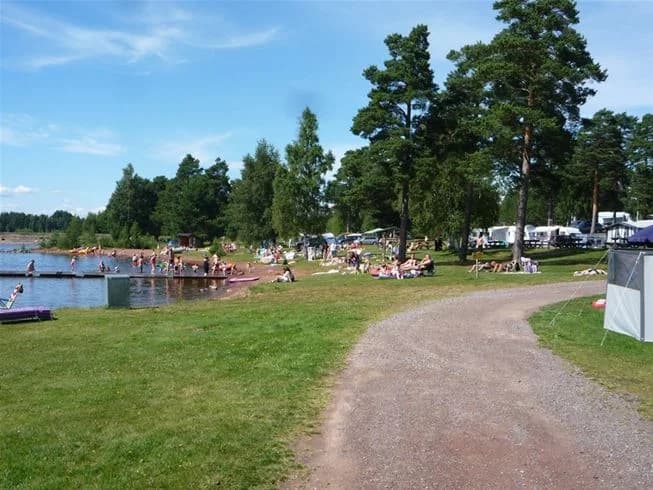 En naturskön campingplats vid en sjö, med skogsklädda stränder och klart vatten, perfekt för rekreation och semesteraktiviteter.