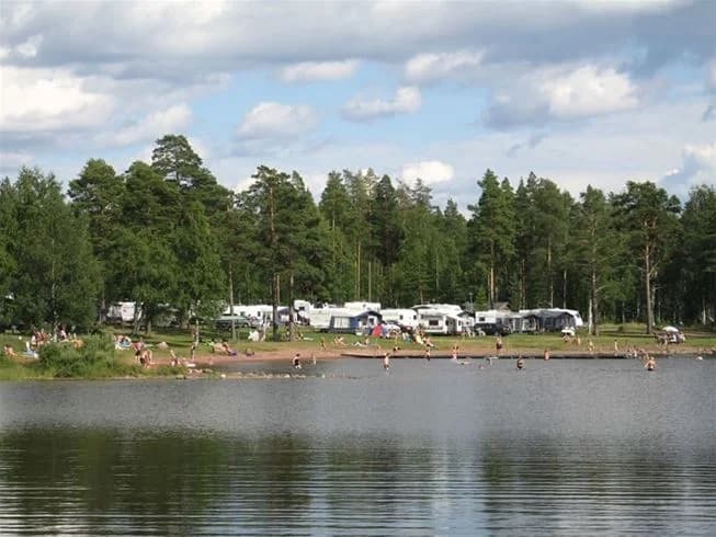 En campingplats vid en sjö, omgiven av grönska och landskap som inbjuder till friluftsliv och rekreation.