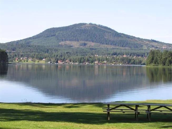 En naturskön vy över Sollerö camping, med en sjö i förgrunden som speglar omgivande kullar och berg i bakgrunden.