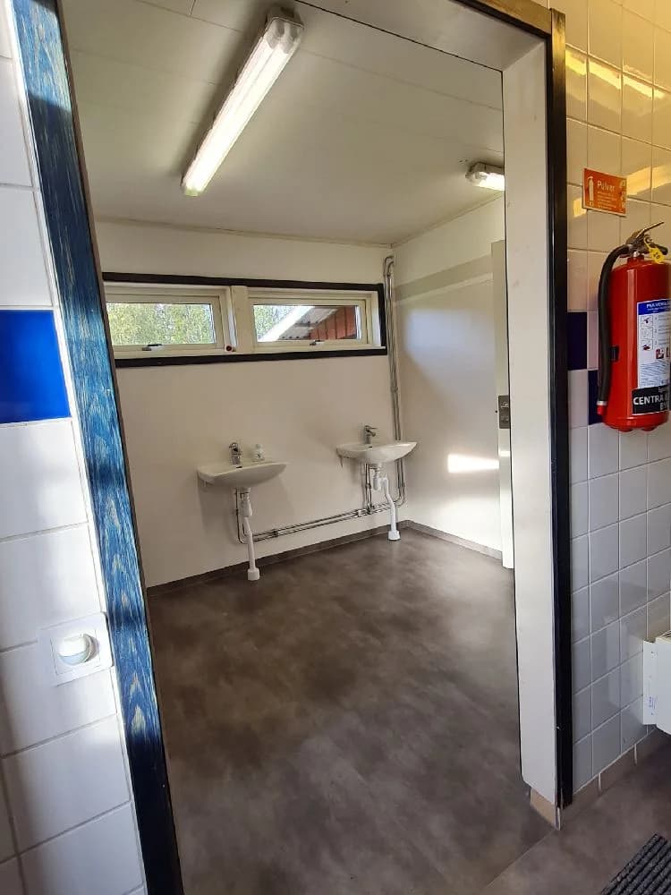 En interiörbild från Särna Camping som visar ett rent och välskött badrum. Rummet har plattor på väggarna, aluminiumdetaljer samt moderna VVS-armaturer.