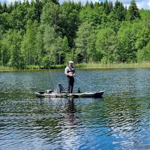 En båt med paddel flyter på en sjö vid Laxsjöns camping, omgiven av frodig natur och lugnt vatten.