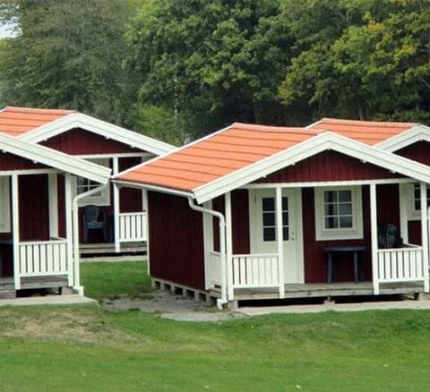En mysig stuga med veranda och sluttande tak omgiven av en lummig trädgård på Marstrands familjecamping.