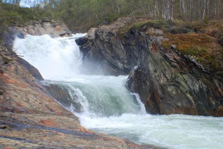 En naturskön bild av en vattenresurs vid Storumans camping, med ett strömmande vattendrag omgivet av klippor och vacker natur.
