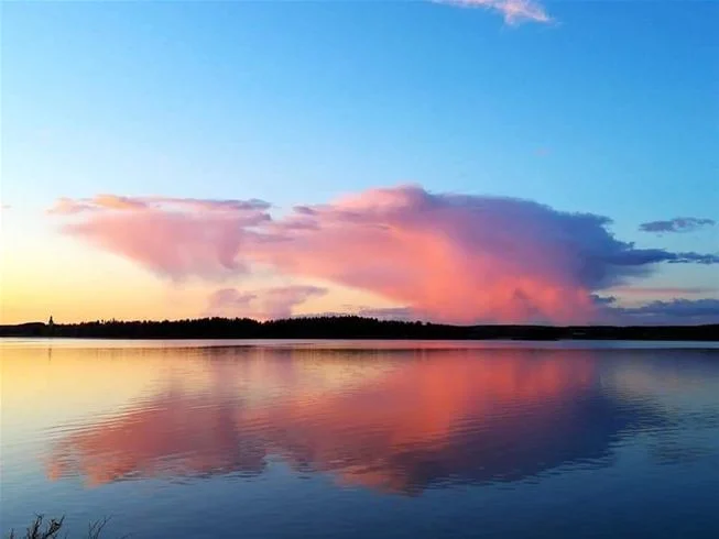 En bild av Falkudden Camping, Café och Stugby med en himmel som skiftar i blått och moln, vatten i horisonten och ett stilla kvällsljus.