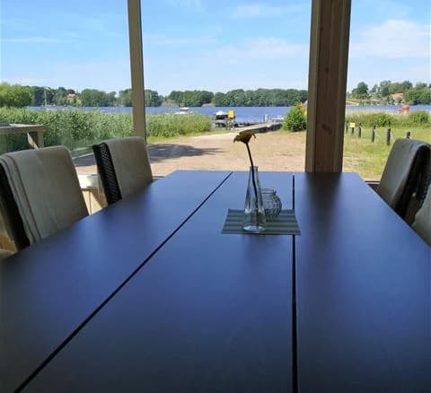 En utomhusmiljö vid Ivö Camping med ett matbord och stolar av trä under en skuggig plats, omgivna av grönska.