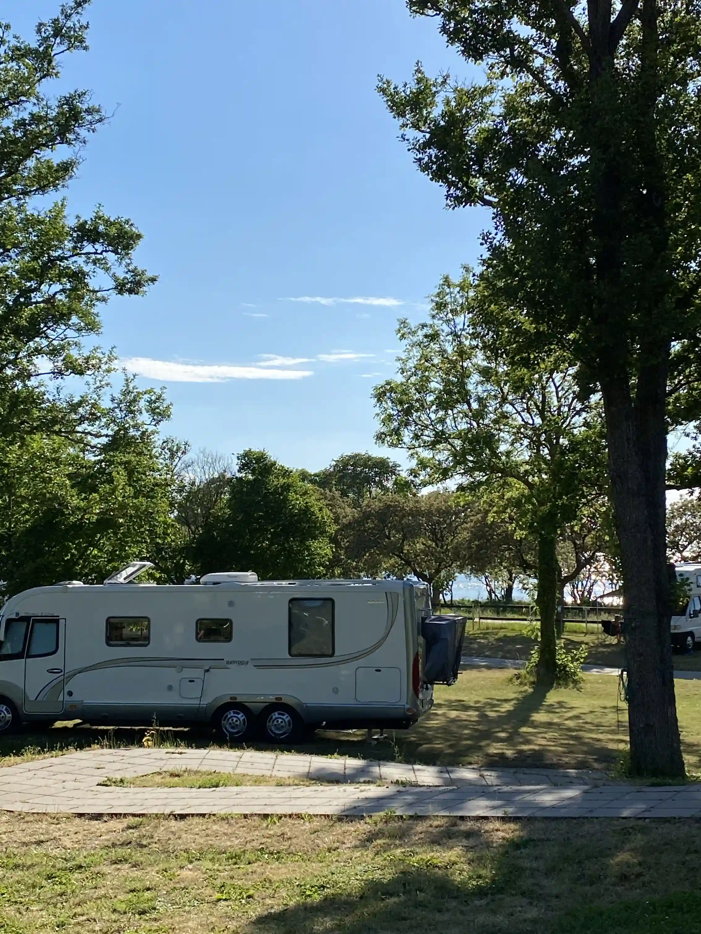 Bild av Kneippbyn Resort Visby som visar en campingscen med husvagnar och husbilar parkerade på en grön yta. Soligt väder med en klarblå himmel i bakgrunden, vilket ger en inbjudande atmosfär för camping och friluftsliv.