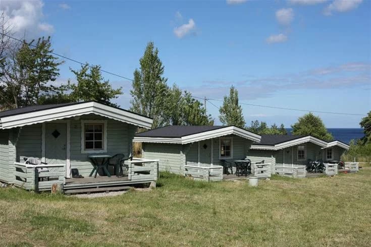 En sommarstuga omgiven av en grönskande trädgård och välskött gräsmatta på Kiviks Familjecamping.