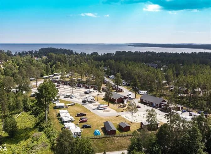 Luftfoto av Sörfjärdens camping som visar en naturskön kustlinje med träd, strand och omgivande ort.