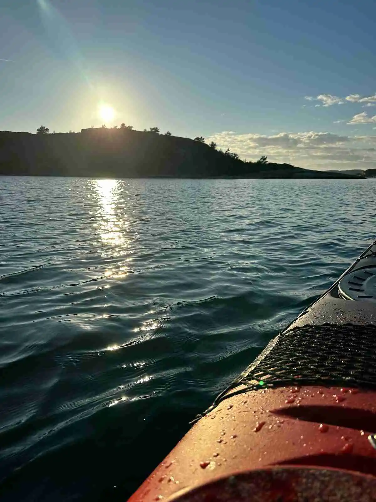 En stilla vattenyta i skymningen med en båt i förgrunden, omgiven av ljusa moln mot horisonten vid Kyrkvikens camping.