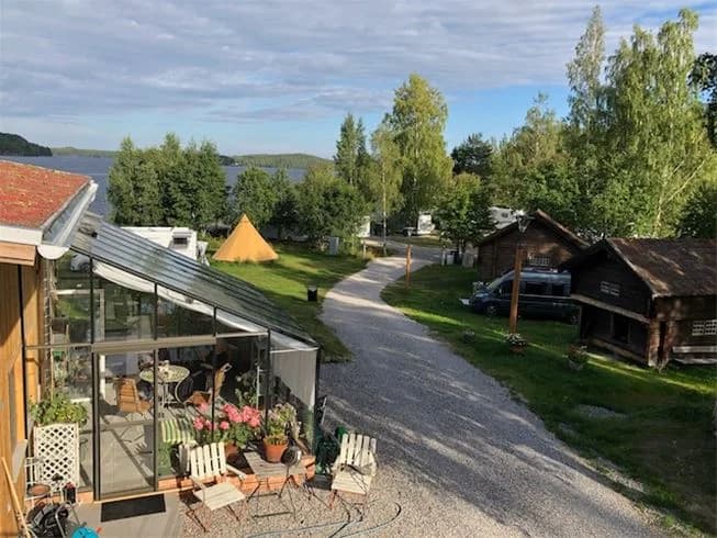 En pittoresk stuga i lantlig miljö, omgiven av välskötta gräsmattor och ett mindre trädgårdsskjul. Den naturnära omgivningen ger en idyllisk och fridfull atmosfär.