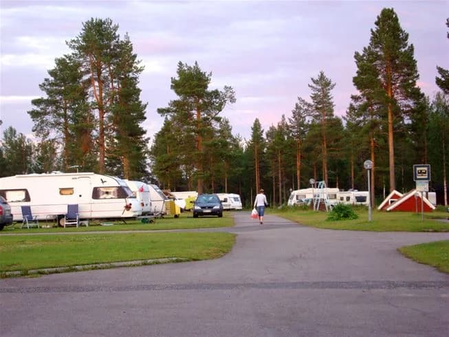 Bild av en husvagn uppställd i en grönskande parkmiljö på Pajala Camping Route 99, med träd och gräsmattor som skapar en avkopplande och naturnära atmosfär.
