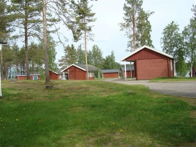 En röd stuga med grästak står på en gräsmatta i ett lantligt område vid Pajala Camping Route 99.