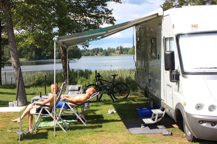 En campingplats i Malmköping med husvagn och cyklar, omgiven av utemöbler och skuggiga träd, som erbjuder avkoppling och friluftsaktiviteter.