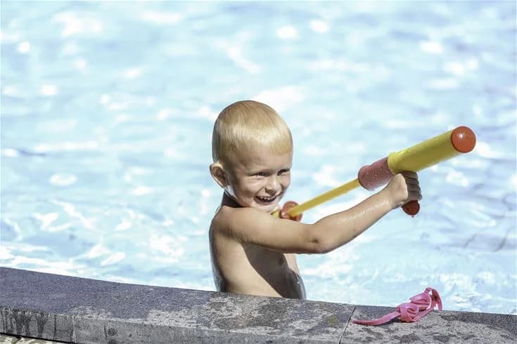Bild på Tånga Heds Camping där barn leker och har roligt vid en swimmingpool. Fritidsaktiviteter pågår och det är en avslappnad semesteratmosfär.