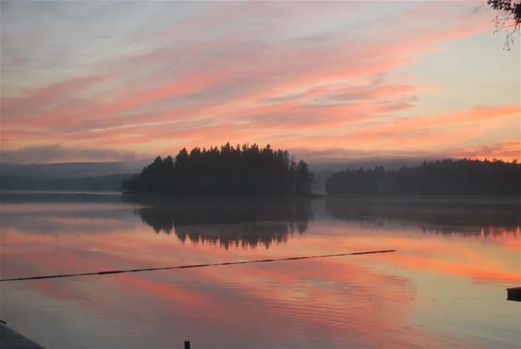 En naturskön vy över en sjö vid solnedgången på Sölje camping, där himlen färgas i varma toner och reflekteras i det stilla vattnet.