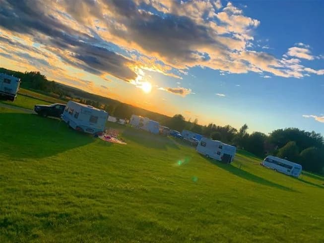 Sommarlandskap vid Sannabadet med grön gräsmatta under en blå himmel med lätta moln i horisonten.