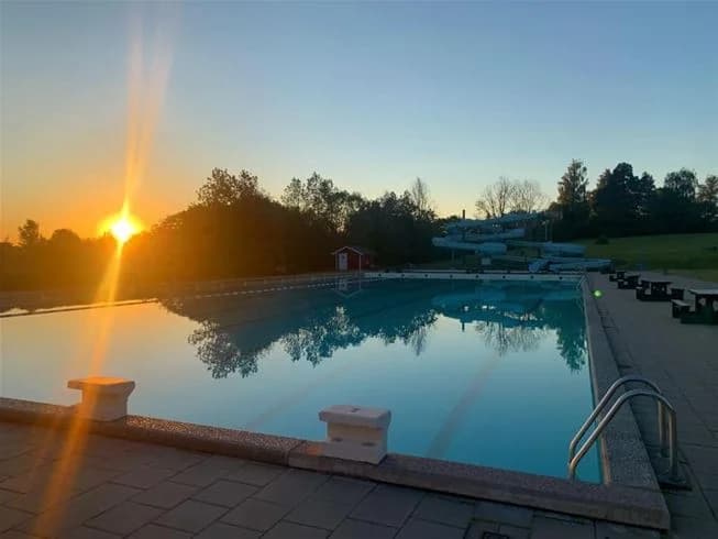 En stor swimmingpool vid Sannabadet belyst i kvällsljus, omgiven av gröna områden och resortliknande faciliteter, vilket skapar en avkopplande rekreationsmiljö.