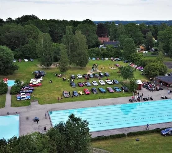 Bild av Sannabadet: människor njuter av fritid och bad vid en pool i en semesteranläggningsmiljö, omgiven av grönska och rekreationsområden.