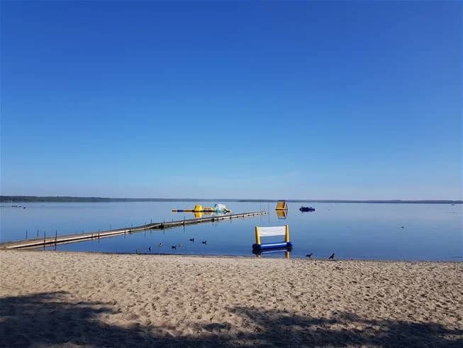 Utsikt över Norje Boke Camping med en blå horisont över havet i bakgrunden. En strandlinje med hav och kustlinje syns, och området framhäver rekreationsmöjligheter vid vattnet.