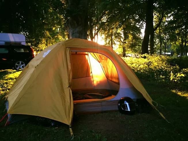 En campingplats vid Norje Boke Camping med flera tält uppsatta på gräsmark, omgivna av träd och campingutrustning, vilket ger en känsla av friluftsliv och avkoppling i naturen.