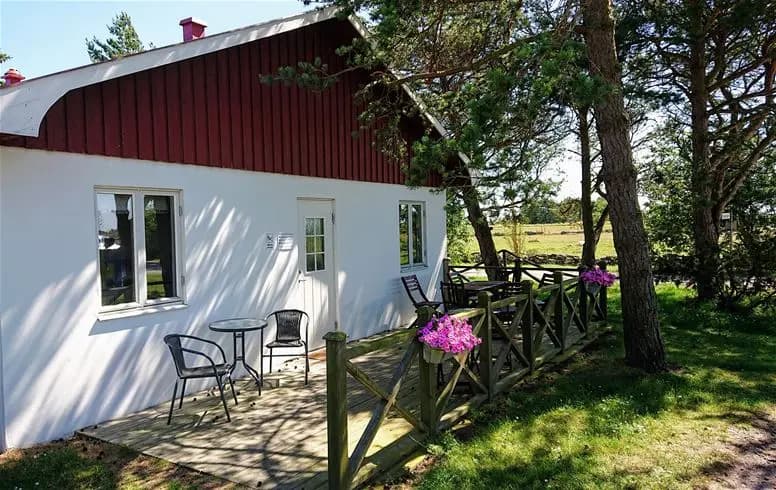 En vit stuga med brunt tak och fönster, omgiven av en grönskande trädgård på Stenåsa Stugor & Camping.