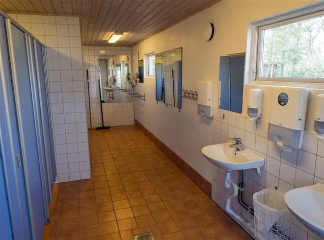 En interiörbild av ett rum på Stenåsa Stugor & Camping. Rummet har träinredning och trägolv, med synliga takbjälkar av trä. I rummet finns även en dörr och inredning som ett handfat. Den naturnära trädesignen skapar en varm och inbjudande atmosfär.