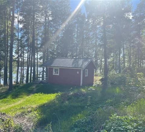 En grönskande campingplats med gräs och träd, där flera små stugor med träfasader och sluttande tak står utspridda.