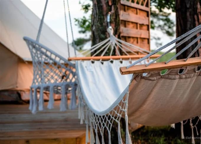 En trädhängmatta med repupphängning står vid en campingplats i Kalmar, omgiven av naturliga material och utomhusmöblering.