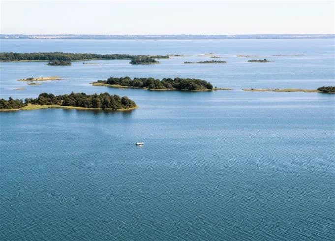 Vy över Kalmar camping - Rafshagsudden, med en kustlinje som sträcker sig längs vattnet. Naturliga element som hav, öar och skärgård syns i bakgrunden.