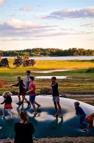 En barnfamilj njuter av sommarvädret vid stranden på Kalmar camping - Rafshagsudden, omgiven av grönska och vatten.