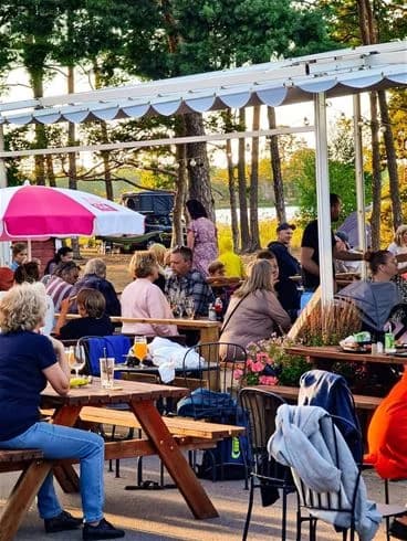 En solig dag på Kalmar Camping - Rafshagsudden med campinggäster som njuter av avkoppling runt utomhusmöbler, inklusive stolar och bord, med parasoller som skyddar mot solen.