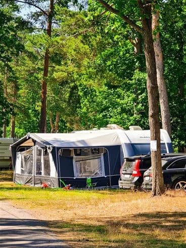 En campingplats vid Rafshagsudden i Kalmar med tält och husbilar uppställda. Det finns en parkeringsplats i närheten och en park med träd. En presenning och ett solskydd är uppsatta för att skapa skugga.