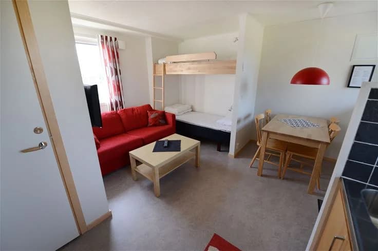 En enkel och inbjudande sovsal med trägolv, möblerad med flera sängar, stolar och ett skrivbord, vilket skapar en hemtrevlig och funktionell miljö för gäster.