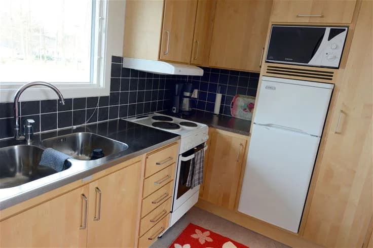 Bild på ett modernt kök vid Gullbrannagården, med en bänk av trä, vita skåp, en kökskran och en diskho. Golvet är av trä och det finns flera köksapparater synliga.