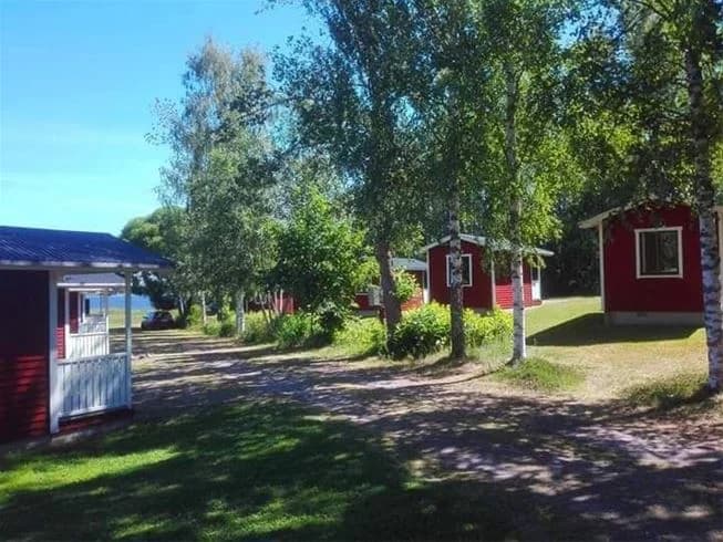 En grönskande campingplats med stugor som omges av välskötta gräsmattor och trädgårdar under skuggande träd. Perfekt för avkoppling i naturen.
