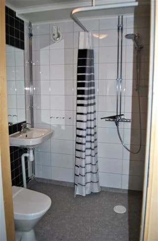 En välordnad badrumsmiljö på Gullbrannagården med ljusa kakelgolv, en toalett med sits, ett handfat med kran och modern inredning.