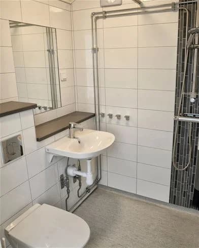 Bild av ett badrum på Gullbrannagården med ett modernt handfat, golv i ljusa nyanser och en toalett. Inredningen är stilren och ljus.