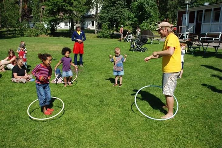 En grupp barn leker med rockringar på en grön gräsmatta vid Gullbrannagården en solig vårdag.