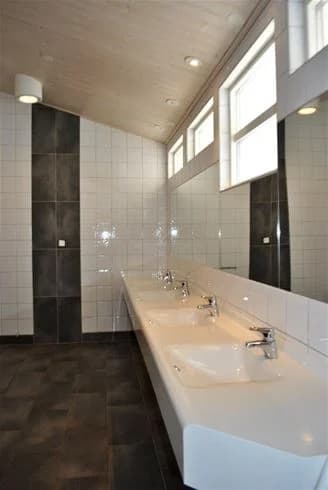 Badkar med kaklade väggar och klinkergolv i badrum på Gullbrannagården. Rummet har ett handfat, takbelysning och moderna sanitetsartiklar, vilket framkallar en fräsch och stilren atmosfär.