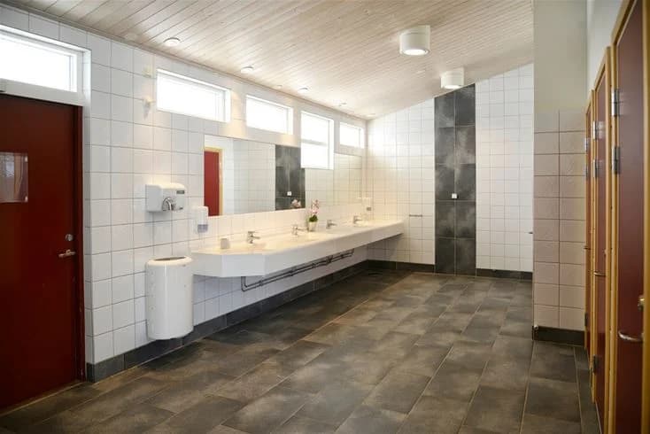 Ett modernt och stilrent badrum med kaklade väggar och golv. Rummet innehåller sanitetsutrustning som en toalett och ett handfat, med diskret belysning från taket.