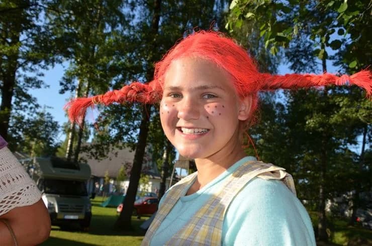 En grupp glada människor klädda i färgglada peruker och dräkter, som skrattar och njuter av tiden tillsammans på Gullbrannagården.