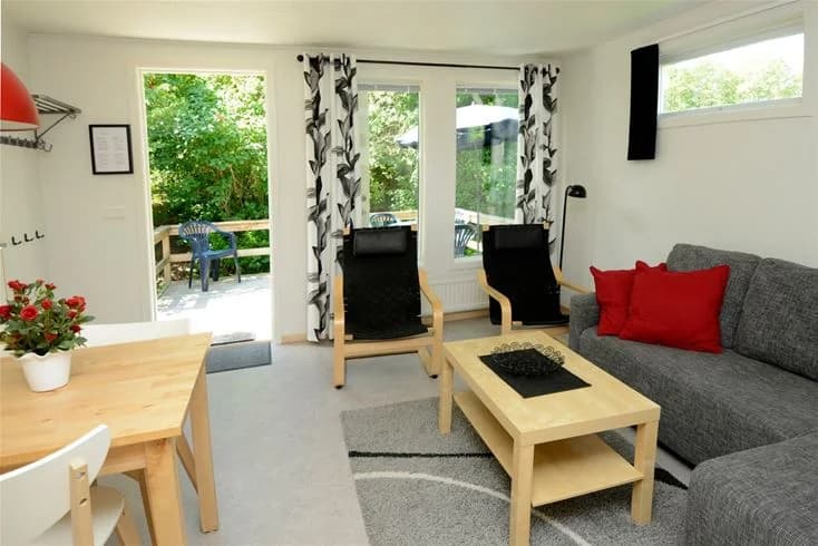 En inbjudande salong med träinredning på Gullbrannagården. Rummet innehåller en soffa, flera stolar och ett träbord på ett trägolv, med tak i matchande trädesign.