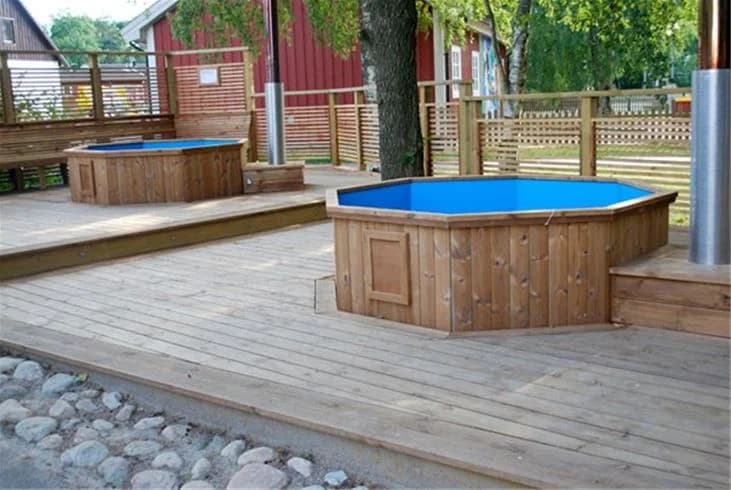 En träveranda med utemöbler och en pool i bakgrunden på Gullbrannagården. Verandan är omgiven av träplankor och grönska.