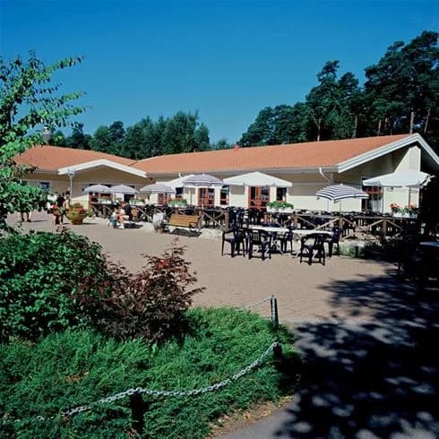 Bild av en utomhusrestaurang på Gullbrannagården med utemöbler under stora parasoller, perfekt för en avkopplande stund i skuggan.