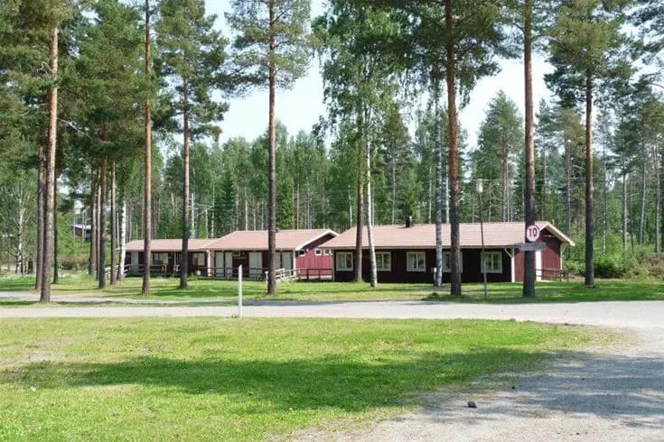 En grönskande campingplats med gräs, träd och stugor vid Vivstavarvstjärns camping. I bakgrunden syns ett lantligt bostadsområde.