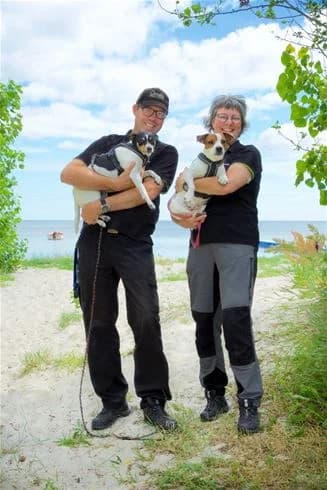 En glad hund sitter bredvid semesterpackning med väskor och stövlar, omgiven av en avslappnad atmosfär vid Stenåsa Stugor & Camping.